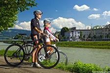 Zwei Radfahrer stehen am Ufer der Salzach und bestaunen die gegenüberliegende Salzburger Altstadt.