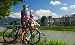 Zwei Radfahrer stehen am Ufer der Salzach und bestaunen die gegenüberliegende Salzburger Altstadt.