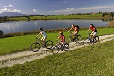 Eine Familie imt zwei Kindern radelt auf einem weiß geschotterten Radweg am Staffelsee entlang.