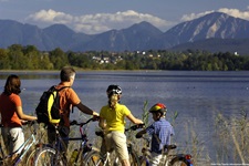 Eine Familie mit zwei Kindern steht am Ufer des Staffelsees und schaut auf die ihn umrahmenden Berge.