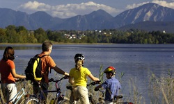 Eine Familie mit zwei Kindern steht am Ufer des Staffelsees und schaut auf die ihn umrahmenden Berge.