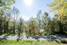 Zwei Radler sind bei strahlendem Sonnenschein auf dem Alpe-Adria-Radweg unterwegs.