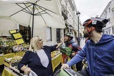 Ein Radlerpärchen wird von einer Marktfrau verköstigt.