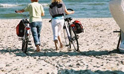 2 Radlerinnen schieben ihre Räder über einen Sandstrand auf die Ostsee zu.