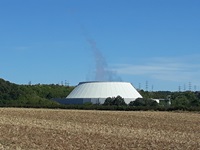 Blick über ein abgemähtes Feld und eine dahinter liegende Biogasanlage