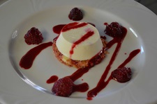 Ein appetitlich auf einem Teller angerichtetes Dessert-Törtchen mit Fruchtsauce und Himbeeren.