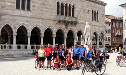 Eine Radlergruppe posiert vor einem Gebäude mit einer männlichen Statue in Udine