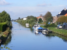 Kanal im Grünen mit angelegten Booten und Häusern im Hintergrund
