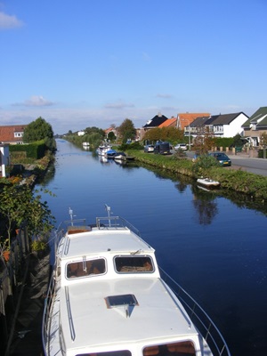 Blick über einen Fluss mit angelegten Booten zu einem Dorf am Ijsselmeer