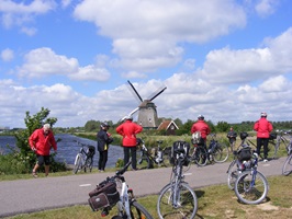 Eine Radlergruppe macht Pause an einem Weg und blickt zu einer der zahleichen Windmühlen in Friesland
