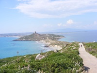Ein einsamer Radler fährt auf den vom Meer umrahmten Turm von Capo Caccia zu.