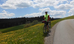 Ein Radler macht neben einer blühenden Wiese Pause und genießt den herrlichen Ausblick über den Südschwarzwald.