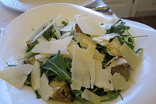 Eine gefüllte italienische Nudelspezialität ist zusammen mit Rucola und Parmesankäse-Stücken appetitlich auf einem weißen Teller angerichtet.