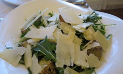 Eine gefüllte italienische Nudelspezialität ist zusammen mit Rucola und Parmesankäse-Stücken appetitlich auf einem weißen Teller angerichtet.