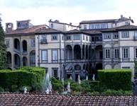 Ein wunderschöner Garten mit Marmorstatuen und grünen Hecken vor einer prächtigen italienischen Villa mit Arkaden.