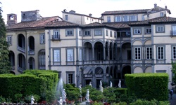 Ein wunderschöner Garten mit Marmorstatuen und grünen Hecken vor einer prächtigen italienischen Villa mit Arkaden.