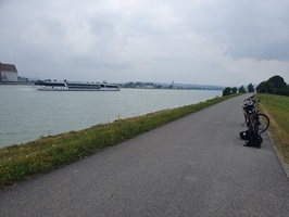 Zwei Fahrräder sind auf dem Donau-Radweg abgestellt und ein Schiff fährt auf der Donau
