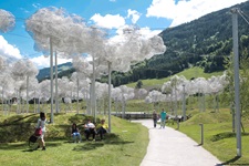 Künstliche, aus Stoff kreierte Wolken schweben an Wäscheleinen über einem kleinen Park.
