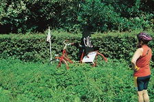 Eine Radlerin steht an einer Kreuzung, an der ein rotes Rad mit einem schwarzen Schild mit der Aufschrift "Café" steht