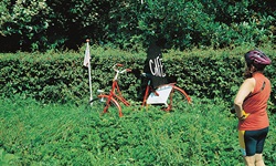 Eine Radlerin steht an einer Kreuzung, an der ein rotes Rad mit einem schwarzen Schild mit der Aufschrift "Café" steht