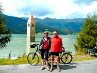 Ein Radlerpärchen posiert vor dem Kirchturm im Reschensee für ein Foto.