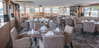 Der Salon mit beigen Stühlen und gedeckten Tischen auf der MS De Holland