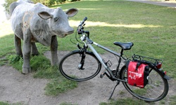 Ein Fahrrad steht neben einer Holzskupltur in Form einer Kuh