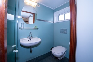 Blick ein hellblau gestrichenes Badezimmer mit Toilette, Waschbecken, Spiegel und Dusche auf der MS Lena Maria