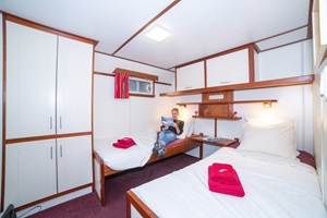 Eine Frau sitzt auf einem Einzelbett in einer Twin-Kabine auf der MS Lena Maria und sieht sich ein Magazin an