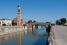 Ein schmucker Kirchturm steht neben einer Brücke über den Flusslauf des Po.