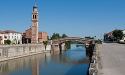 Ein schmucker Kirchturm steht neben einer Brücke über den Flusslauf des Po.