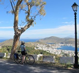 Eine Radfahrerin steht am Straßenrand auf der Insel Patmos und blickt über den Hafen von Skala in der Griechischen Ägäis