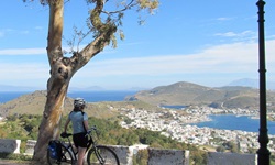 Eine Radfahrerin steht am Straßenrand auf der Insel Patmos und blickt über den Hafen von Skala in der Griechischen Ägäis