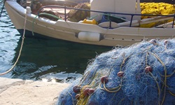 Fischernetze liegen an Land am Hafen und dahinter ist ein angelegtes Fischerboot der Griechischen Ägäis