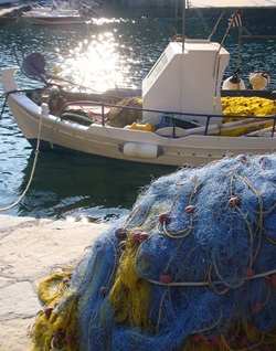 Fischernetze liegen an Land am Hafen und dahinter ist ein angelegtes Fischerboot der Griechischen Ägäis