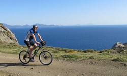 Ein Mountainbiker fährt einen Weg entlang der Südlichen Ägäis - im Hintergrund ist das tiefblaue Meer zu sehen