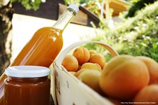 Eine Flasche Marillenlikör und ein Glas Marillenmarmelade neben einem mit Marillen gefüllten Korb.