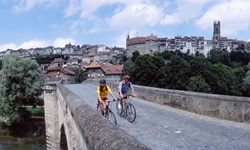 Ein Radlerpärchen übequert auf einer steinernen Brücke bei Freiburg im Üechtland die Aare.