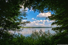 Der Ammersee durch ein von Bäumen gebildetes Fenster gesehen.