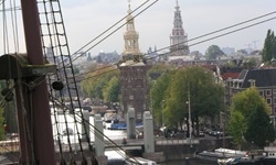 Blick auf das Zentrum von Amsterdam; im Vordergrund die Takelage eines Segelschiffs.