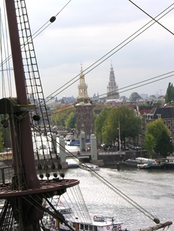 Blick auf das Zentrum von Amsterdam; im Vordergrund die Takelage eines Segelschiffs.