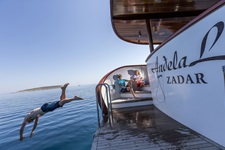 Ein junger Mann springt von der Badeplattform am Heck der Andela Lora ins Meer und wird dabei von zwei anderen Passagieren beobachtet.