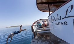 Ein junger Mann springt von der Badeplattform am Heck der Andela Lora ins Meer und wird dabei von zwei anderen Passagieren beobachtet.