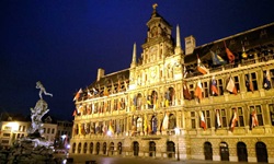 Das mit verschiedenen Fahnen geschmückte Stadthuis (= Rathaus) von Antwerpen wird nachts von Scheinwerfern angestrahlt.
