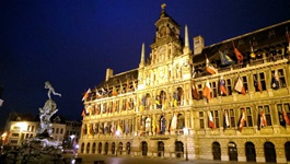 Das mit verschiedenen Fahnen geschmückte Stadthuis (= Rathaus) von Antwerpen wird nachts von Scheinwerfern angestrahlt.