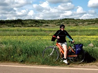 Eine Radlerin ruht sich am Straßenrand vor einer wunderschön blühenden Wiese aus.