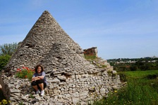 Eine Radlerin macht bei einem alten apulischen Steinhaus, einem Trullo, Pause und genießt die herrliche Landschaft.