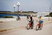 Zwei Radlerinnen radeln am Meer entlang und genießen das typische Flair eines apulischen Küstenortes.