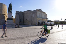 Ein Radfahrer und mehrere Fußgänger passieren das Denkmal für die 800 Märtyrer in Otranto.