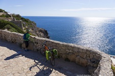 Ein Radfahrer blickt von einer Küstenstraße im Salento auf das tief blau schimmernde Meer hinaus.